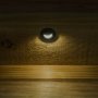 A round mini LED step light with black metal trim ring and hood on installed on a wooden deck