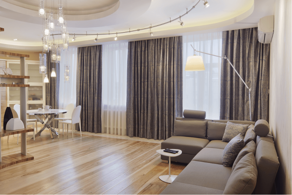 Modern living room with grey couch, large windows, and dining table